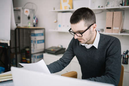 Office worker reading paperwork in the office. Focused employee wearing glasses and reading documents in coworking space.の写真素材