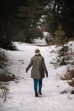Lonely woman walking on snowy winter road. View from back of a girl walking alone on snowy road among trees in cold winter day.の写真素材