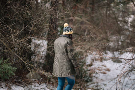 Tourist girl on snowy road in park. Woman wearing knitted hat and green jacket walking on snowy alley in the park.の写真素材