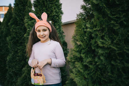 Happy young girl in bunny ears holding basket with eggs