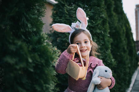 Happy little girl holding stuffed toy and basket with eggs