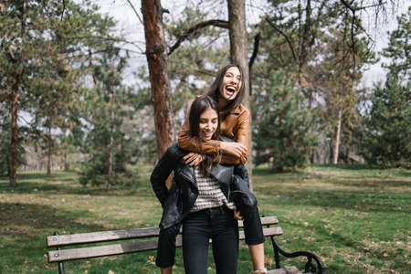 Smiling girl carrying her sister through parkの写真素材