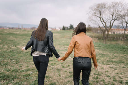 Slim women walking in the park and holding hands. Back of girls in fashion clothes holding hands while walking in the park.の写真素材