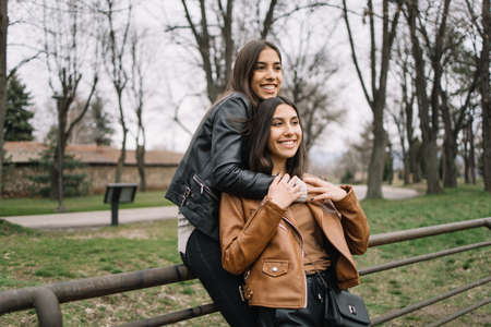 Female friends cuddling while leaning against fenceの写真素材