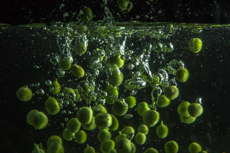 Green peas falling into water with black background