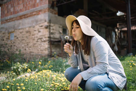 Young woman squatting in garden and blowing dandelionの写真素材