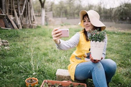 Happy girl holding pot with flower and taking selfieの写真素材