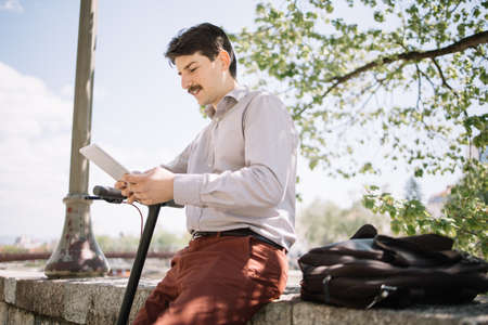 Young entrepreneur man sitting on fence and looking at tablet