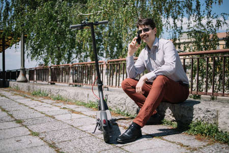 Young man having conversation on smartphone while sitting near fenceの写真素材