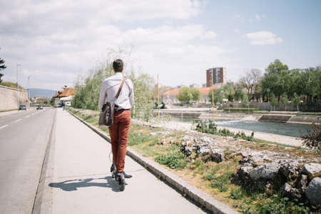 Back of man on electric electric scooter driving on riverside roadの写真素材
