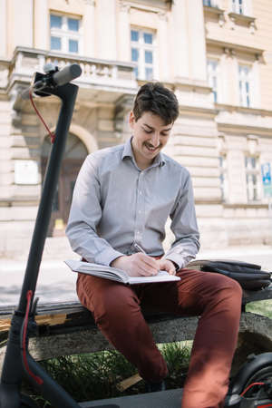 Happy man in shirt writing in notebook outdoorの写真素材