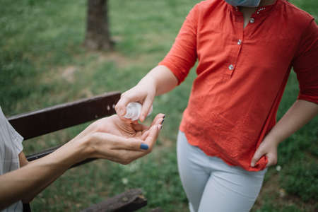 Cropped people disinfecting hands with antiseptic spray in park. Childs hands applying hand sanitizer to disinfect female hands during virus pandemic.の写真素材