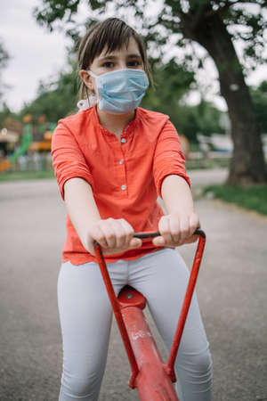 Close-up of young girl at the payground, using mask. Young girl playing in the public park wearing antivirus mask during the COvid-19 pandemic, frontviewの写真素材