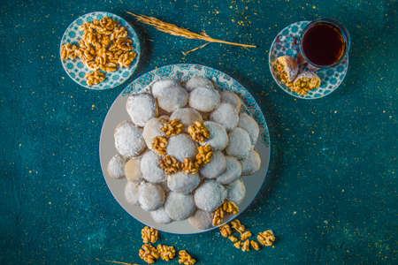 Top view of butter cookies with powdered sugar and walnuts. Biscuits covered with powdered sugar arranged in serving platter on table next to plate with walnuts and cup of tea.の写真素材