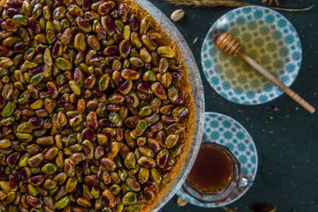 Cropped pistachio dessert above plate with honey and cup of tea. Cake with pistachios on stand with blurred honey dipper and tea in background.の写真素材