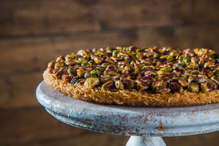 Cake stand with oriental dessert with pistachio against wooden background. Arabic sweet dessert of kadayif and pistachios on stand against wooden background.の写真素材