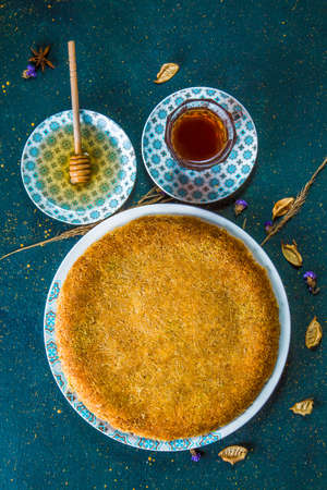 Oriental dessert of kadaif noodles on table with honey and tea. Turkish sweet cheese pastry with honey on table with cup of tea and honey dipper.の写真素材