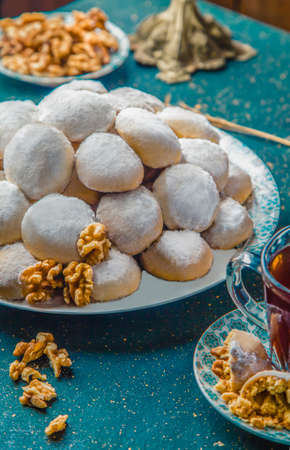 Close-up view of biscuits covered with powdered sugar. Butter cookies with powdered sugar and walnuts on blue table with tea and walnuts.の写真素材