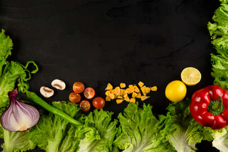 Top view of vegetables arranged on black table with center copy space. High angle view of lettuce on black surface with mushrooms, tomatoes, cut onion, corn and pepper on black surface with empty space in center.の写真素材