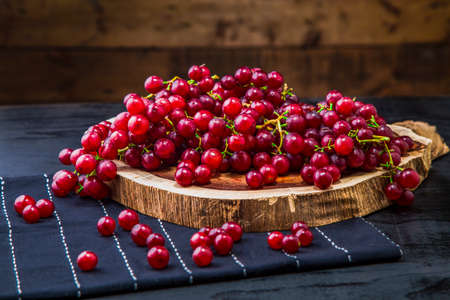 Scattered grape berries on wooden slice and table. Red grape berries arranged over wooden board on table with table runner and wooden background.の写真素材
