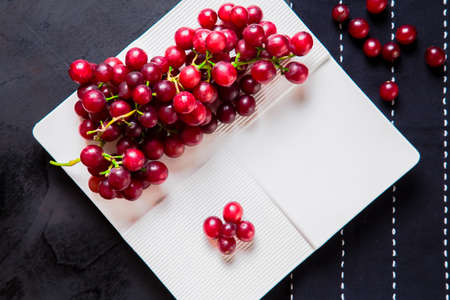 Top view of fresh grapes arranged in plate. Close-up of fresh mellow red grapes arranged in white plate on table with table runner and scattered berries.の写真素材