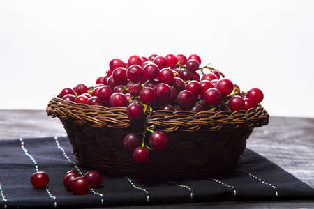 Wicker basket with grapes on table runner with white background. Bowl with fresh red grape berries on table runner with white background.の写真素材