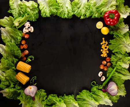 Lettuce arranged in shape of frame on black surface with vegetables. Lettuce arranged in square shape with chopped mushrooms, tomatoes, cut onion, corn and pepper on black surface with empty space in center.の写真素材