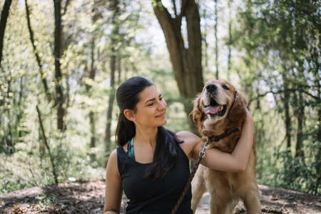 Portrait of smiling girl and happy dog. Cropped girl hugging her dog while sitting in the park during sunny day.の写真素材