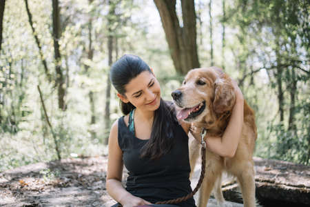 Cropped woman hugging dog in the park. Young woman in black top sitting in forest and cuddling her dog.の写真素材