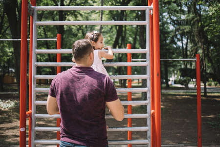 Dad and his daughter having fun in playground. Little girl climbing facilities in playground while father is holding her.の写真素材