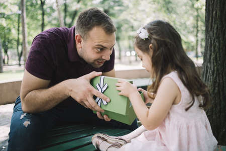 Little girl looking in opened present in her fathers hands. Surprised dad opened a present and his...