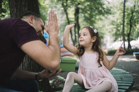 Dad and child giving high five outdoor. Daughter and her doing high five gesture while sitting on bench in park.の写真素材