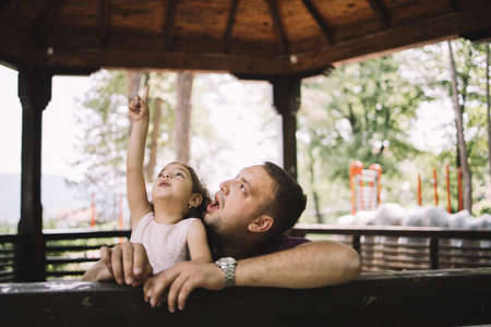 Daughter and father having fun in wooden gazebo. Little girl hand pointing while standing with her dad in wooden pavilion in nature.の写真素材