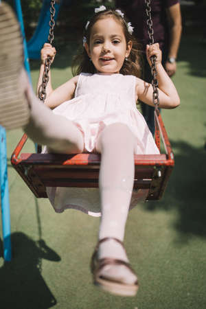 Portrait of cute little girl swinging in park. Little girl swaying on swing in front of cropped man in playground.の写真素材