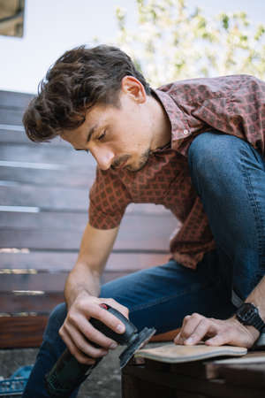 Young man using polish machine on wooden board. Portrait of male worker using polish machine on carpentry work.の写真素材