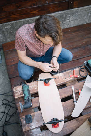 High angle view of worker using screws to make skateboard. Top view of brunette man assembling skateboard parts.の写真素材