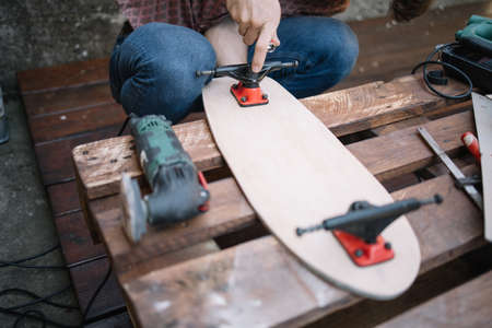 Wooden pallet with skateboard deck, trucks and tools . Cropped man using screwdriver to mount trucks on skateboard deck.の写真素材