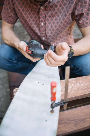 Close-up view of male hands holding power sander and sanding paper. Man putting sanding sheet to electric sander while making skateboard.の写真素材