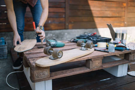 Cropped man assembling skateboard on table in workshop. Males hands making skateboard on pallet in...