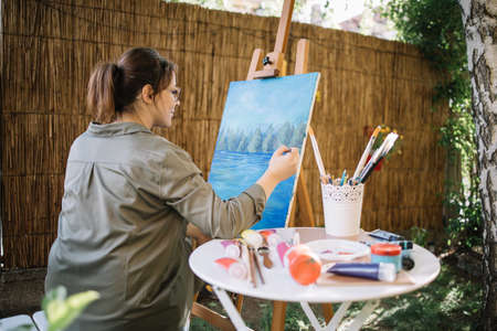 Close-up view of woman setting yard for painting. Female artist preparing wooden stand for adding canvas while squatting in garden.の写真素材