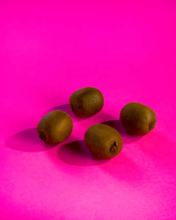 Kiwi fruit on pink surface with shadow. Close-up view of fresh brown kiwis arranged on electric pink surface.の写真素材