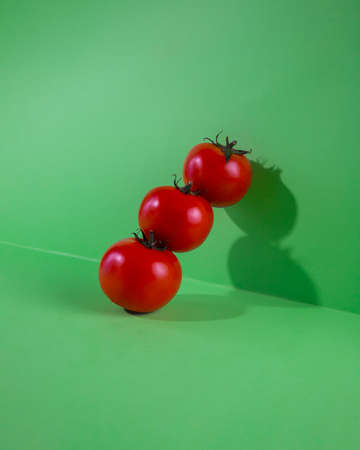 Red fresh tomatoes on green background with shadow. Tomato tower isolated on green background.の写真素材