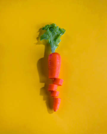 Sliced carrot with lettuce isolated on yellow background. Cut carrot with lettuce arranged in carrot shape on yellow surface.の写真素材