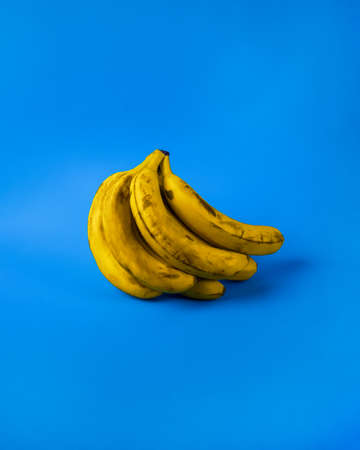 Few aged bananas with dark spots against blue background. Bunch of brown spotted bananas isolated on blue background.の写真素材