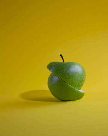Cut green apple isolated on yellow background. Two pieces of cut green apple connected together on yellow surface.の写真素材