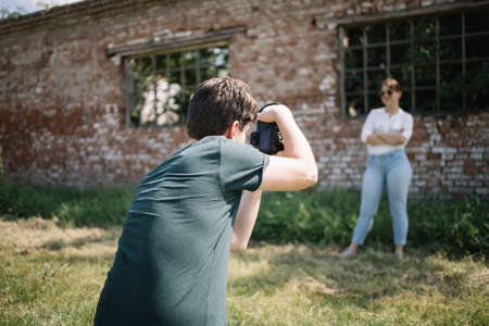 Girl posing in front of old building while man is taking photo of her. Back of photographer taking photos of pretty woman posing in front of old factory.の写真素材