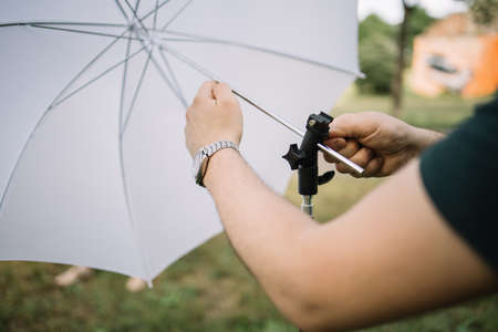 Cropped man setting umbrella diffuser with tripod outdoor. Close-up view of male hands placing umbrella diffuser to tripod in nature.の写真素材