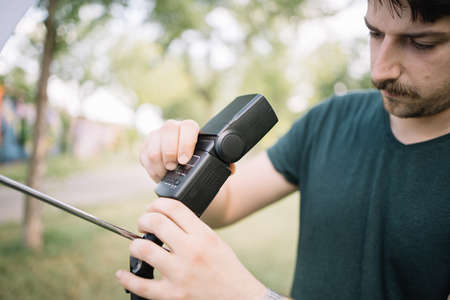 Close-up view of man connecting flash to light stand. Focused man setting umbrella flash to light...