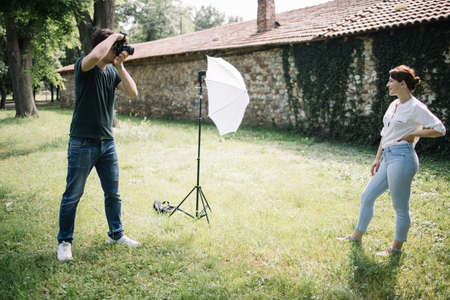 Photographer taking pictures of female model in front of old house. Side view of photographer...