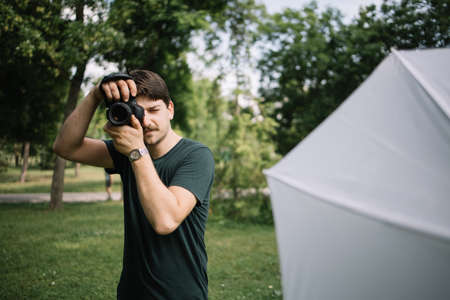 Man taking photos using camera in park. Front view of male photographer taking pictures in nature...